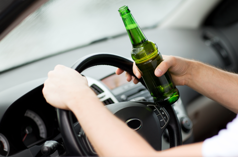 transportation and vehicle concept – man drinking alcohol while driving the car